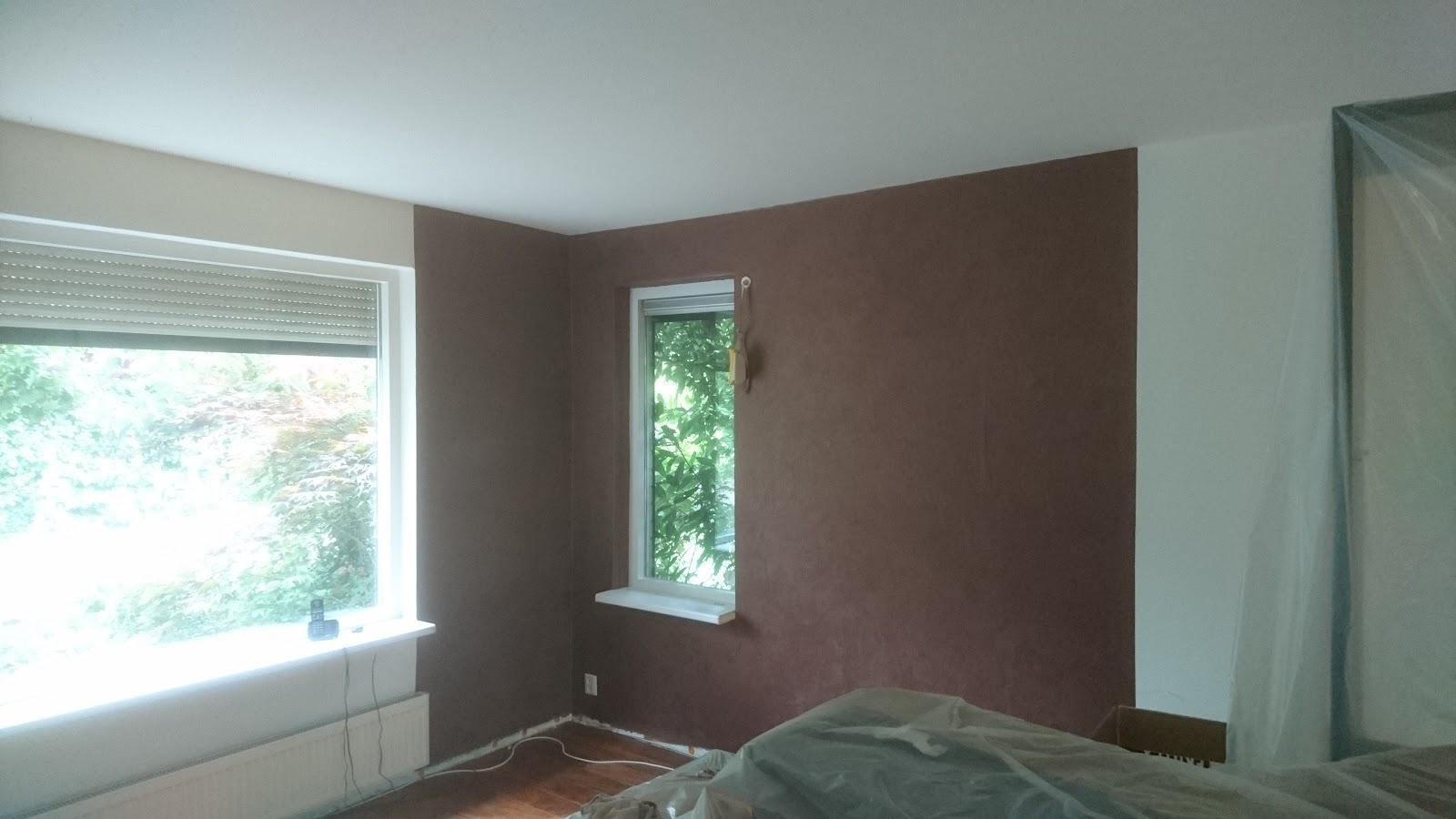 Terracotta accentmuur tijdens binnenschilderwerk, meubels afgedekt met plastic.